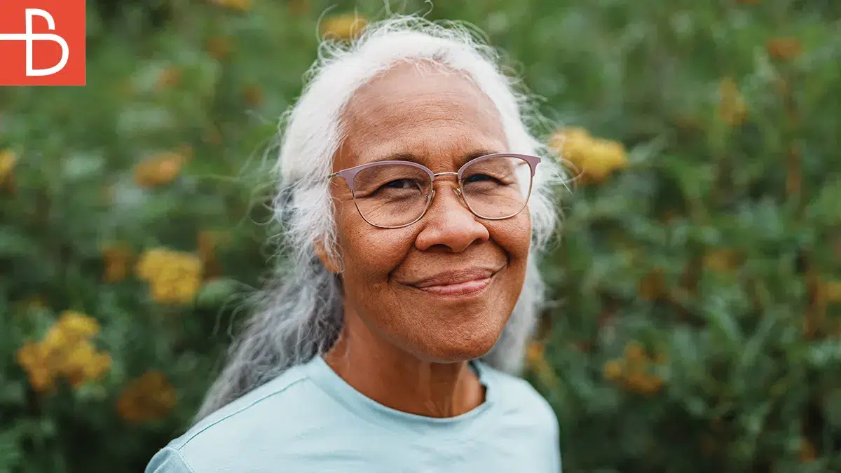 Senior woman with glasses smiling in front of flowers